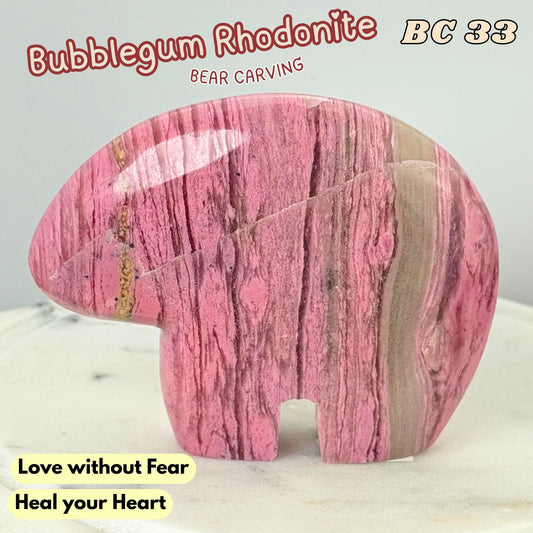 A polished pink rhodonite bear carving with natural marbled veining, displayed on a light marble surface against a pale gray background. Text overlays include 'Bubblegum Rhodonite', 'BC 33', 'Bear Carving', and 'Love without Fear Heal your Heart'.