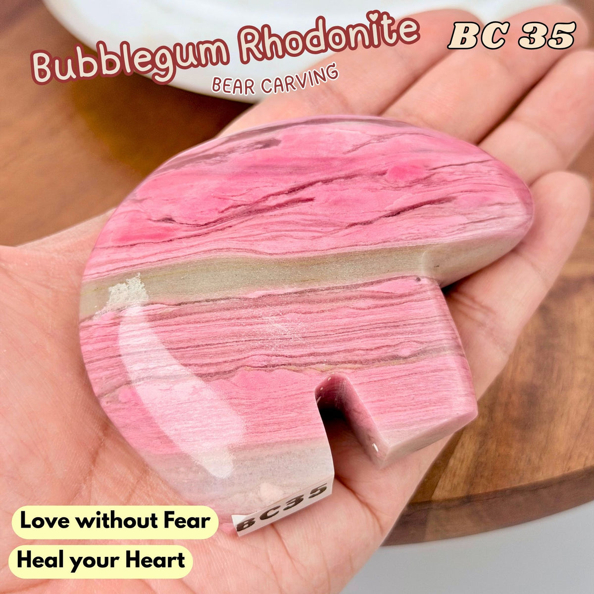 A polished pink rhodonite carving shaped like a bear, held in a person's hand. The stone features natural marbled pink and beige patterns.