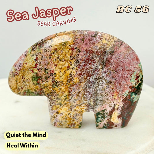 A polished Sea Jasper bear carving with a multicolored pattern of pink, gold, green, and brown, displayed on a light marble surface with text overlays.