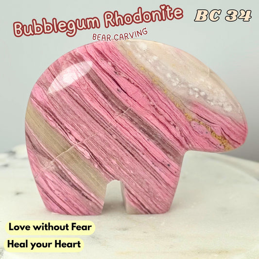 A carved bear-shaped stone sculpture made of pink, beige, and brown striped rhodonite, displayed on a light marble surface with text overlays.