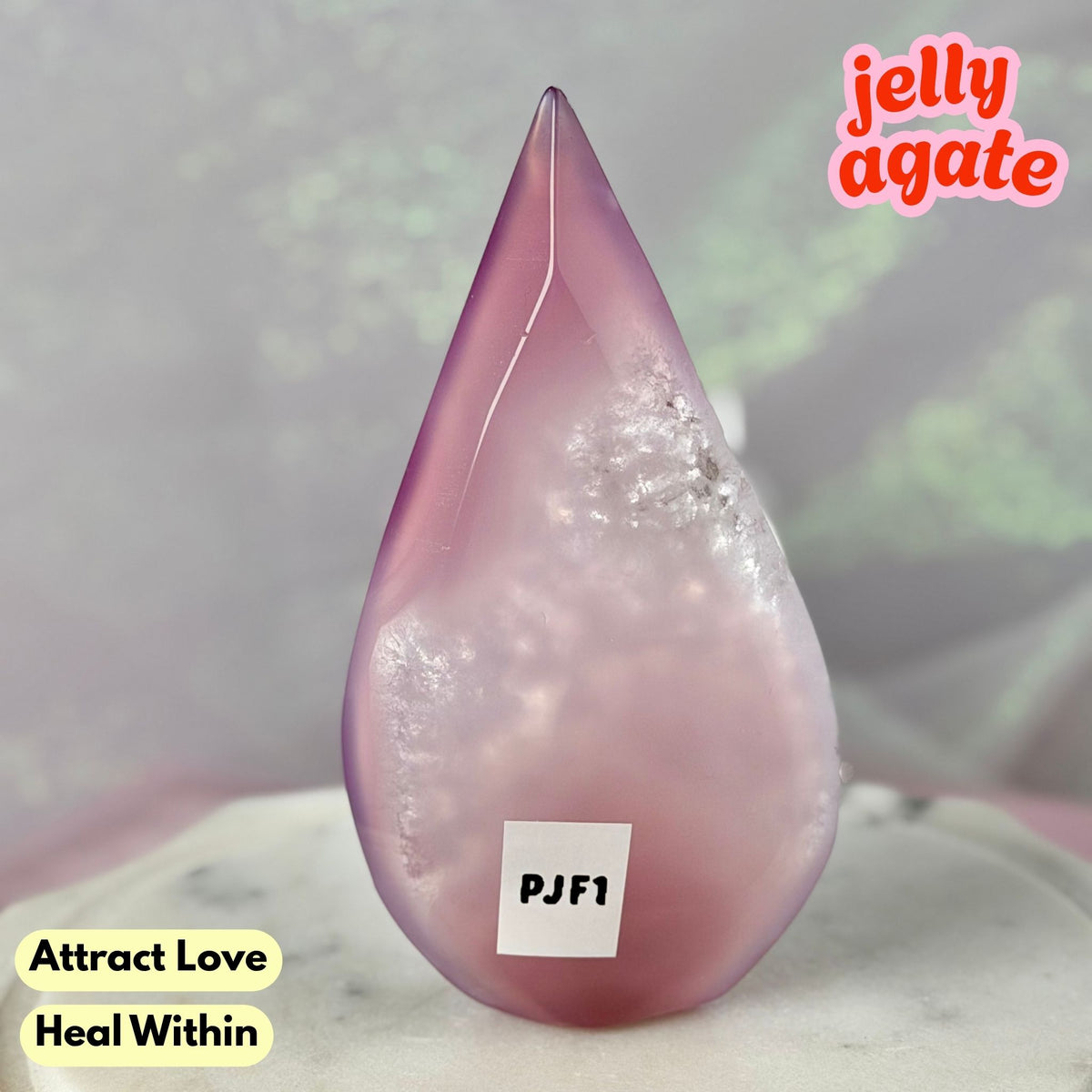 A teardrop-shaped jelly agate crystal with a pink and purple gradient, featuring natural inclusions, displayed on a light marble surface with text overlays.