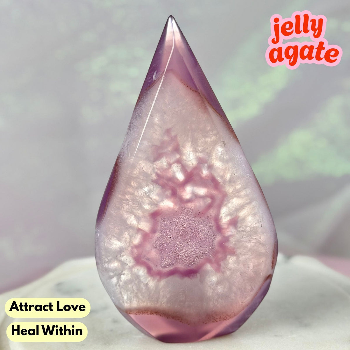 A teardrop-shaped jelly agate crystal with a pink and purple agate pattern inside translucent resin, displayed on a light surface with text overlays.