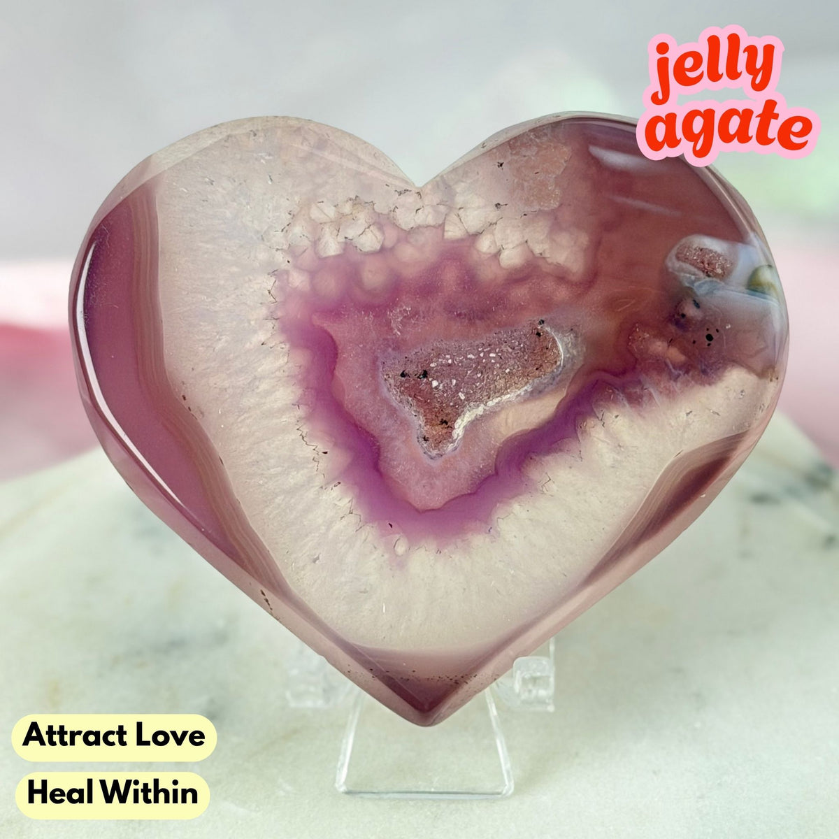 Heart-shaped jelly agate crystal on a clear acrylic stand, featuring a purple and pink geode pattern with white outer bands, displayed on a marble surface with text overlays.