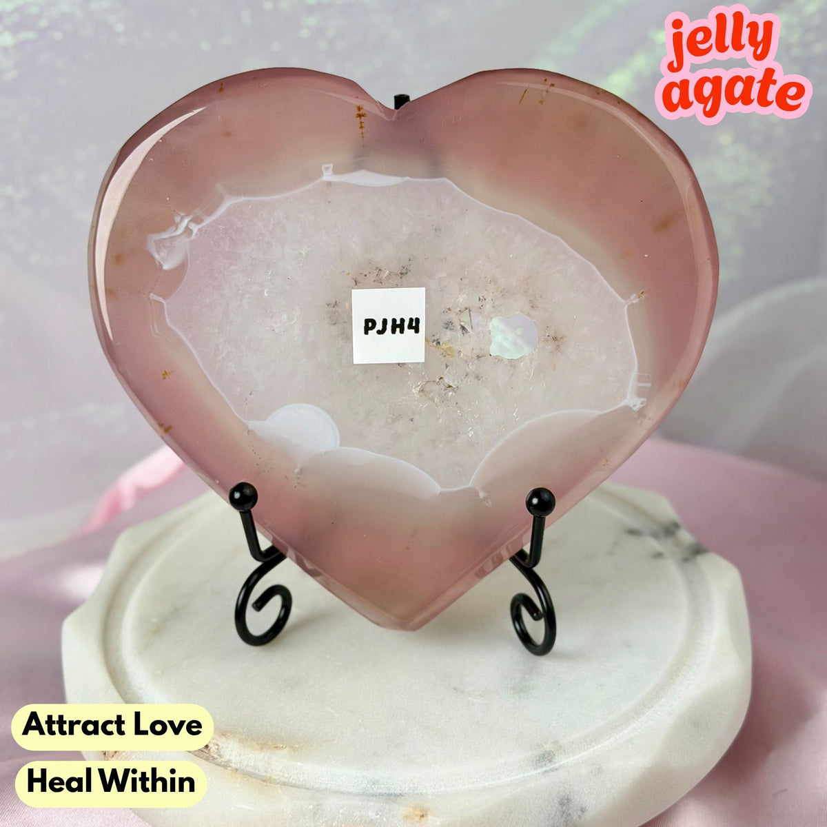 Heart-shaped polished jelly agate crystal display piece on a small black metal stand, set on a round white marble base. The agate has a pinkish-tinted translucent center with natural crystalline edges.
