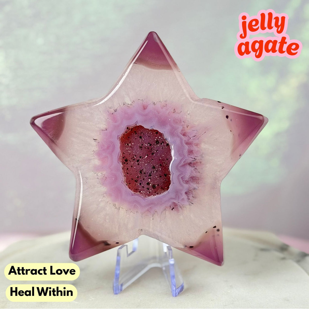 A star-shaped jelly agate crystal display on a clear acrylic stand, featuring a pink and purple agate pattern with a glittery red center. Text overlays read 'jelly agate', 'Attract Love', and 'Heal Within'.