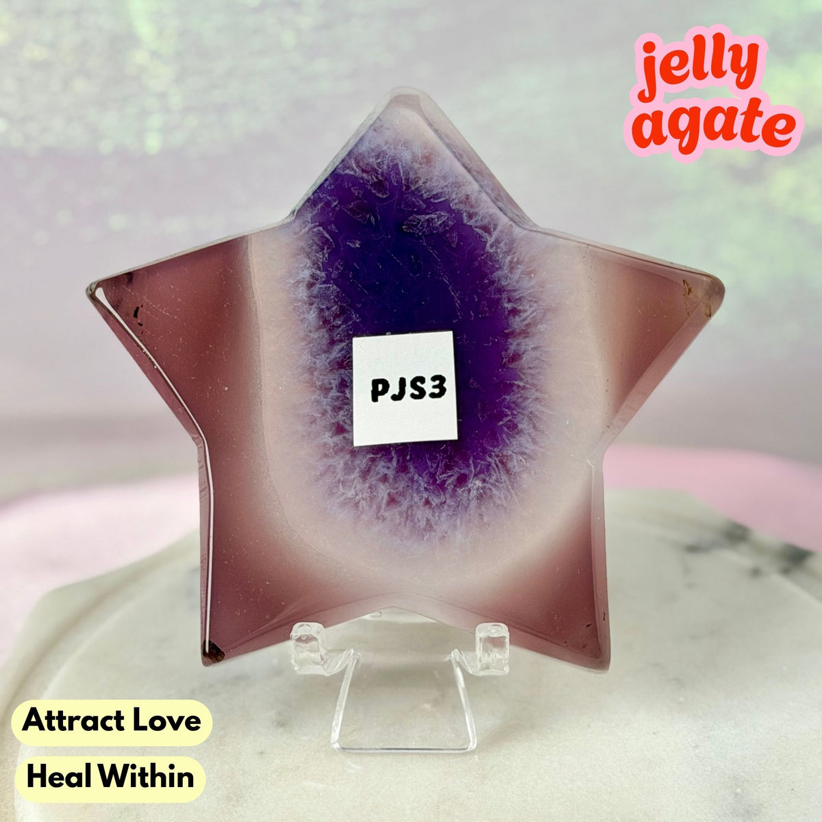 A star-shaped jelly agate crystal display on a clear acrylic stand, featuring a purple and mauve gradient center. The image includes text overlays reading 'jelly agate', 'Attract Love Heal Within', and a label 'PJS3'.