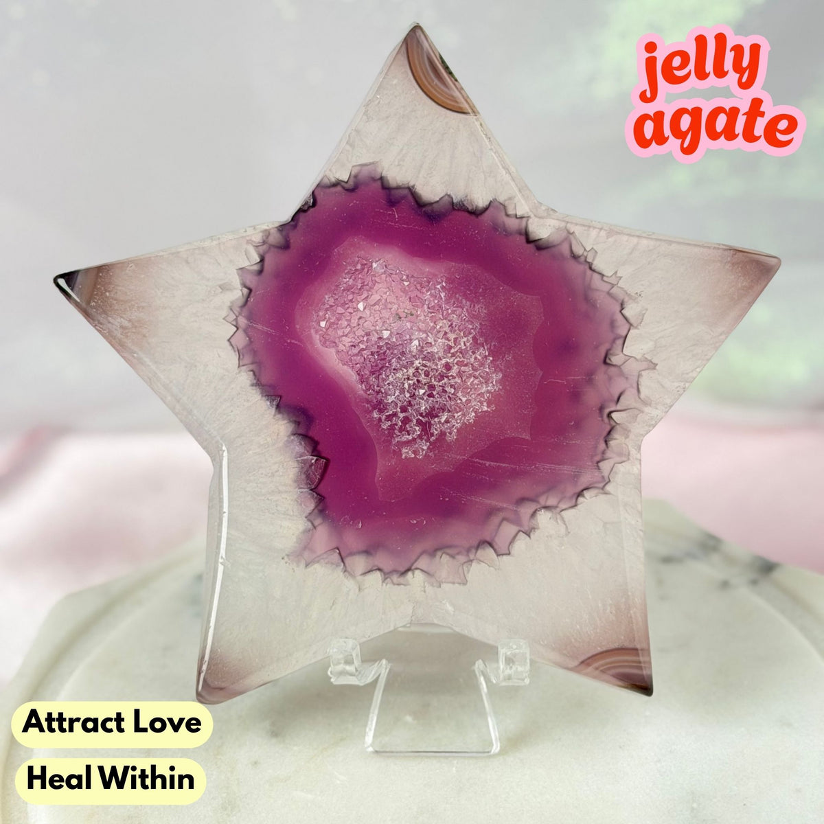 A star-shaped jelly agate crystal display piece on a clear acrylic stand, featuring a vibrant magenta-purple center with white crystalline inclusions and a translucent pale pink outer edge. Text overlays read 'jelly agate', 'Attract Love', and 'Heal Within'.