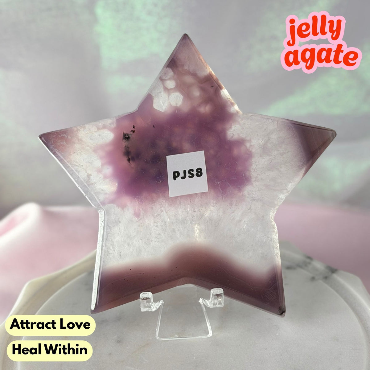 A star-shaped polished jelly agate crystal display piece on a clear acrylic stand, featuring a gradient of purple and white agate patterns. The image includes text overlays 'jelly agate' and 'Attract Love Heal Within'.
