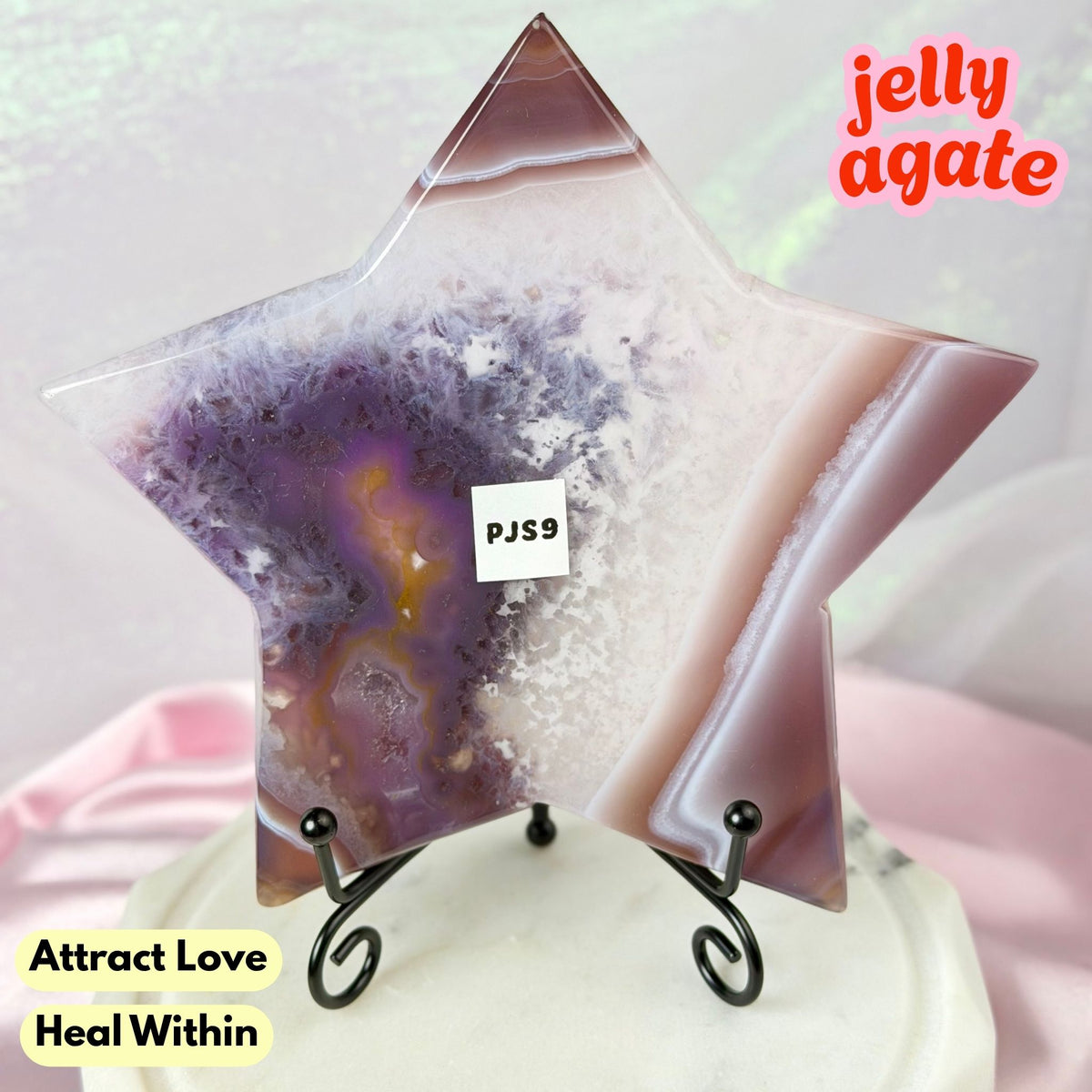 A star-shaped polished jelly agate crystal display piece on a small black stand, with purple, pink, and white agate patterns. Text overlays read 'jelly agate', 'Attract Love Heal Within', and a small 'PJS9' label is visible on the product.