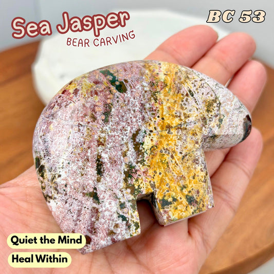 A hand holds a polished sea jasper bear carving with a mottled pattern of yellow, pink, white, and dark green. Text overlays read 'Sea Jasper', 'BEAR CARVING', 'BC 53', 'Quiet the Mind', and 'Heal Within'.