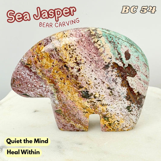 A carved sea Jasper bear figurine with a multicolored marbled pattern of pink, yellow, green, and brown, displayed on a light marble surface against a white background with text overlays.