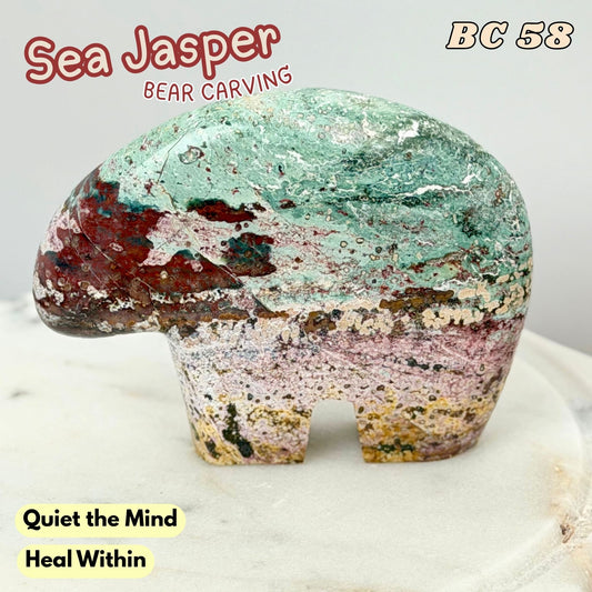 A carved sea Jasper bear figurine with layered natural stone colors, including teal, pink, brown, and cream, displayed on a white marble surface. Text overlays read 'Sea Jasper', 'BEAR CARVING', 'BC 58', and 'Quiet the Mind Heal Within'.