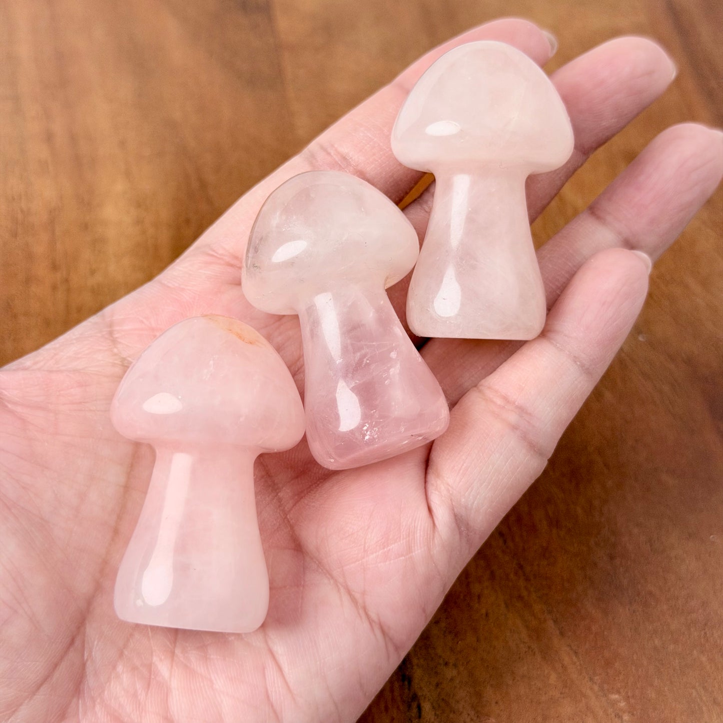 Three small mushroom-shaped rose quartz crystal points resting on an open hand over a wooden surface.
