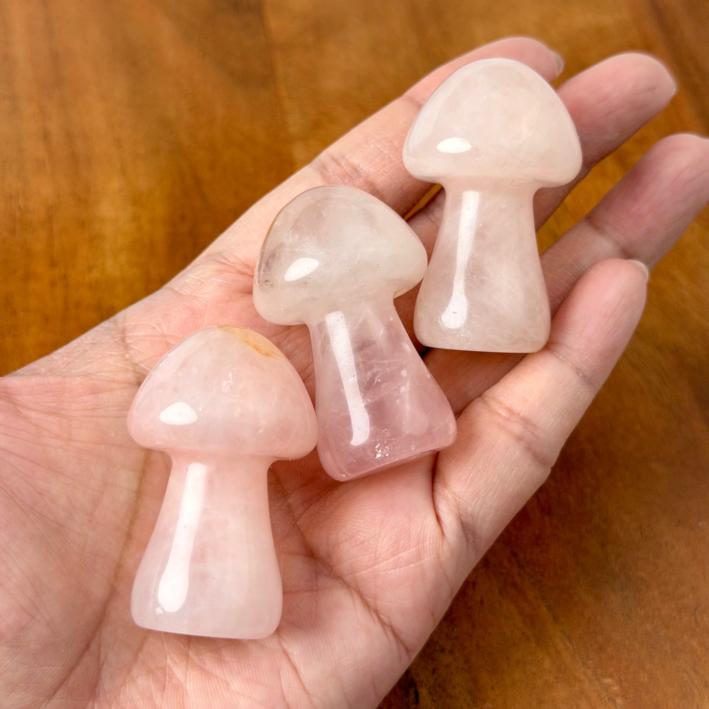 Three small mushroom-shaped rose quartz crystal points held in a person's hand over a wooden surface.